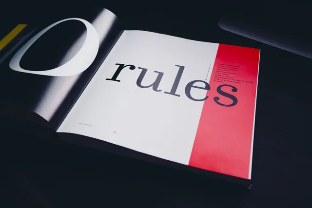 Close-up of an open book page featuring the word 'rules' with a black background. Handing an approved finance creator ad to the publisher